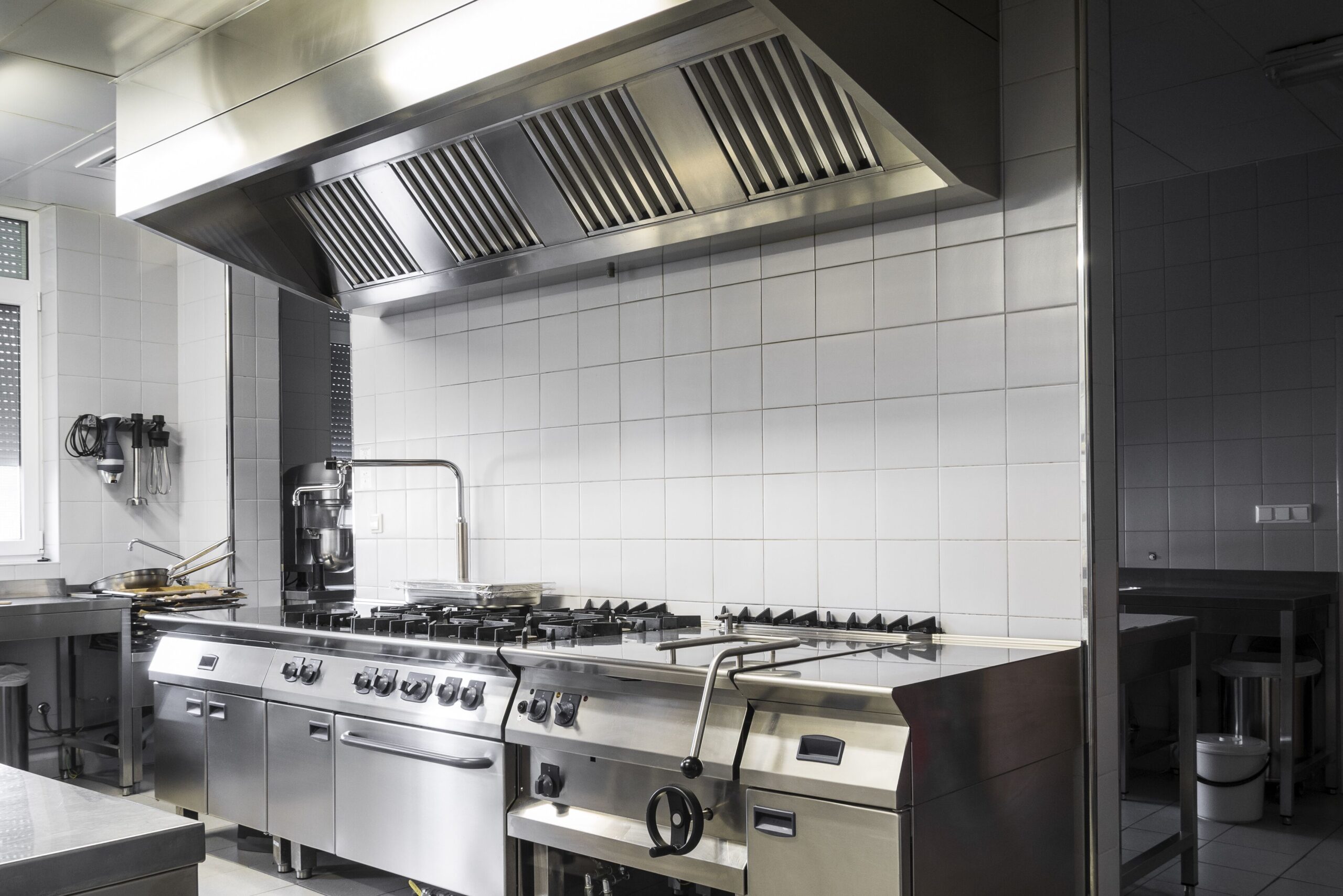A spacious commercial kitchen featuring stainless steel appliances and workstations, designed for food preparation and cooking.