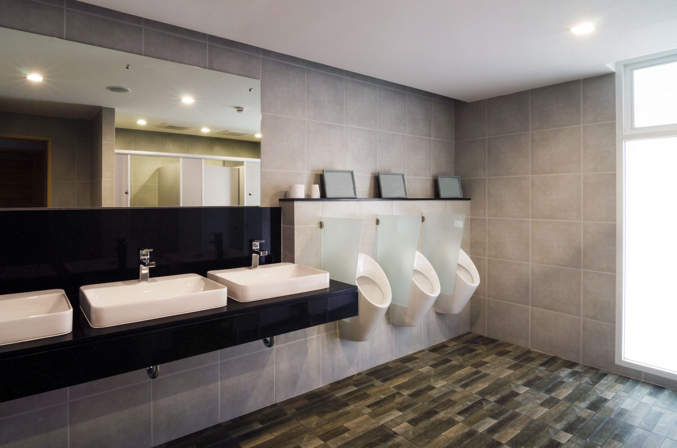 A bathroom featuring three urinals and a single sink, designed for male use.