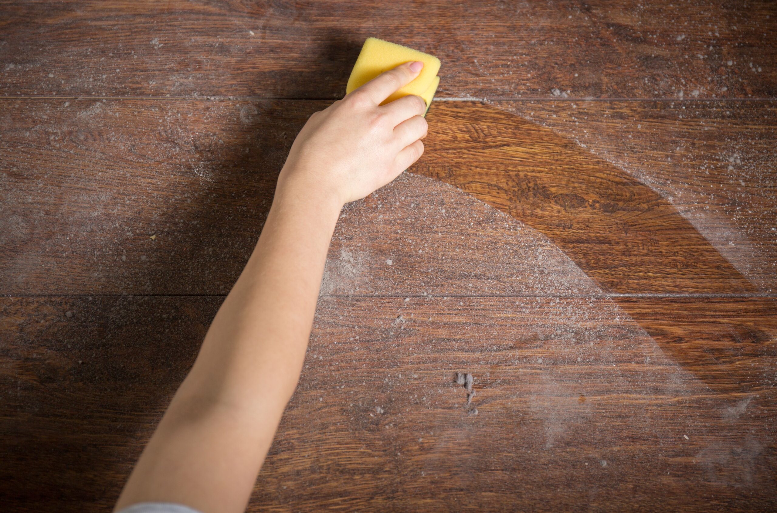 A person using a sponge to clean a wooden floor, demonstrating effective cleaning techniques