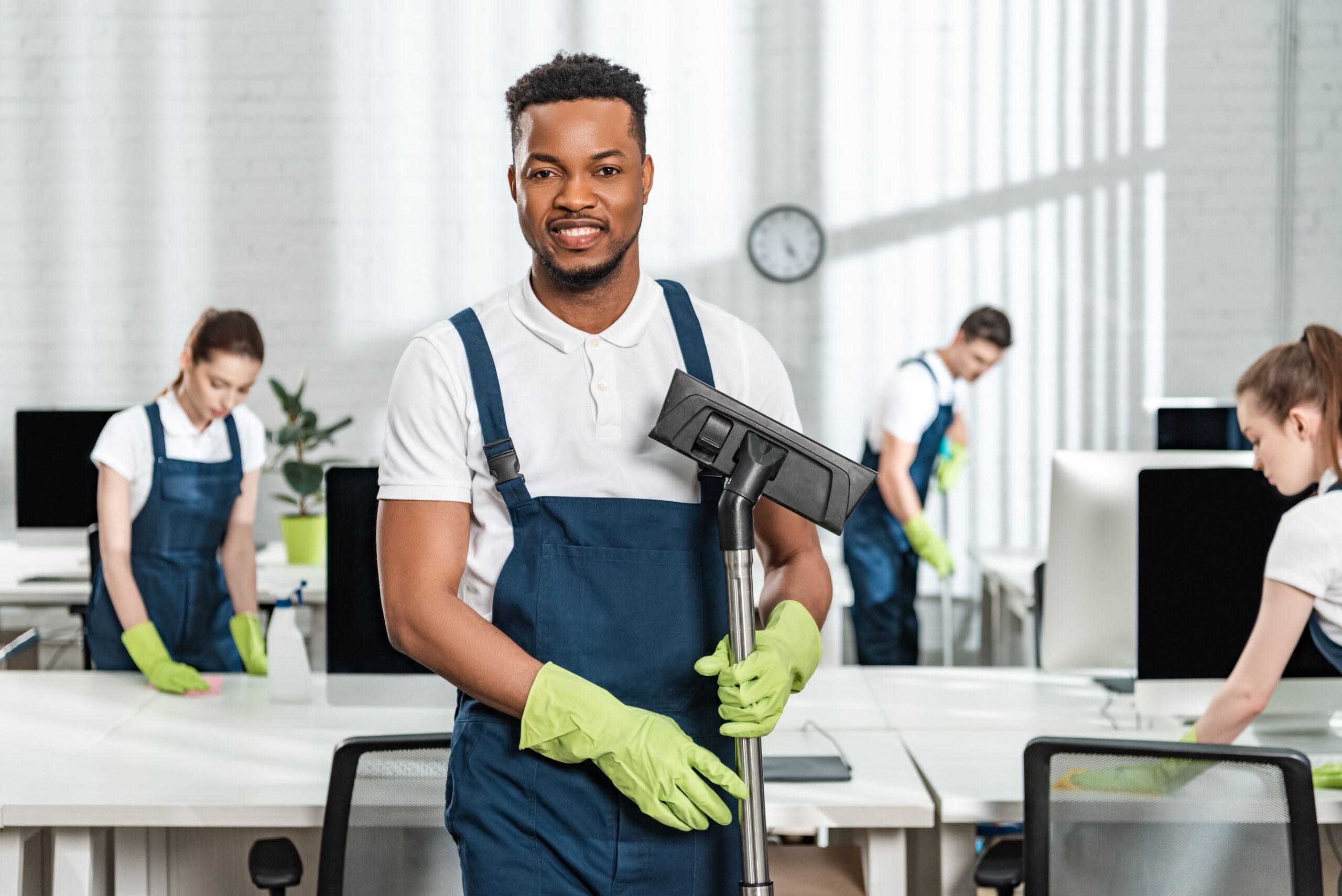 A man wearing overalls and gloves is holding a vacuum cleaner, preparing to clean a surface